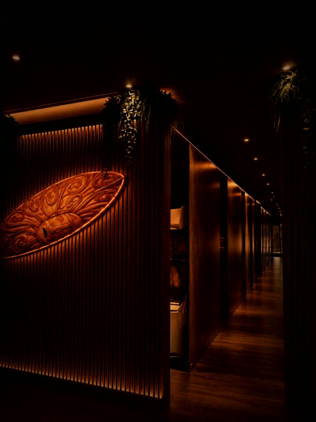 The warm, slatted Tanners Lane corridor — carved artwork, private suites and a glowing doorway beyond